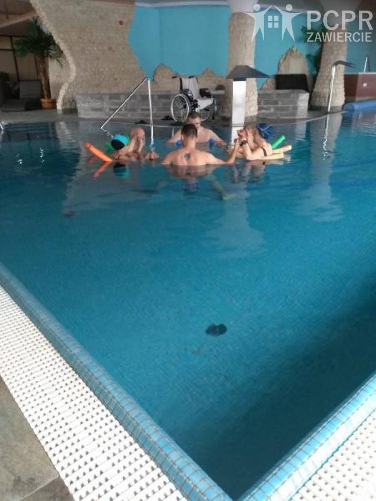 Zdjęcie: Grupa kobiet i mężczyzn w basenie wykonuje ćwiczenia stojąc w kręgu